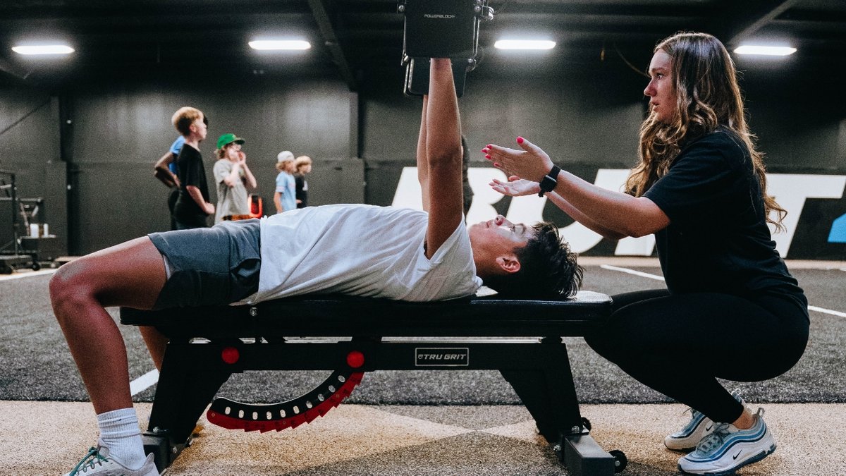 Female trainer helping a young boy with weight bench exercises