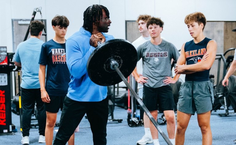 Trainer teaching a group of young boys the proper way to lift weights at the gym
